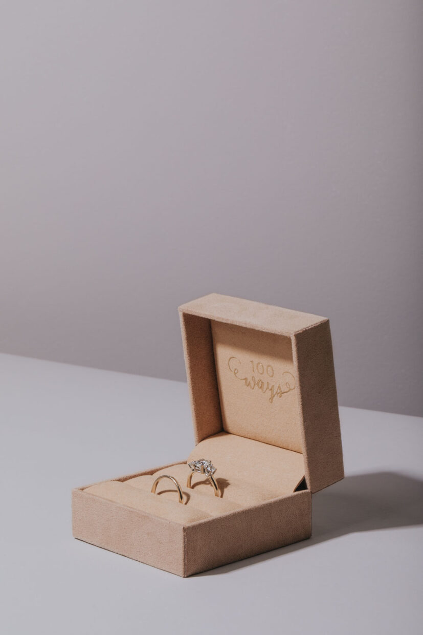 Professional photograph of a jewelry box with a diamond engagement ring inside. Blush coloured velvet wrapped jewelry box with vintage gold rings. Professional product photography